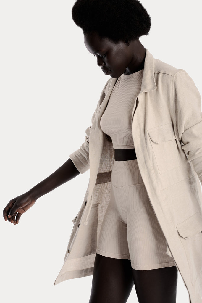 Model wearing sand ribbed biker shorts and a matching sand crop top, and a natural linen jacket, left-side close-up view.