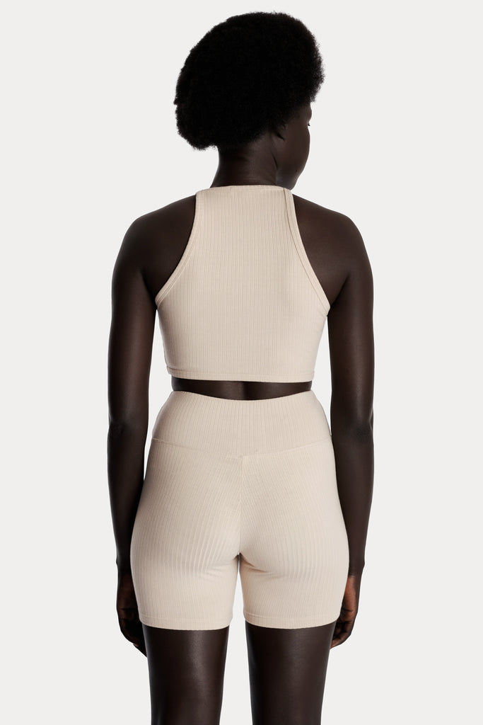 Model wearing sand ribbed biker shorts and a matching sand crop top, back-side close-up view.