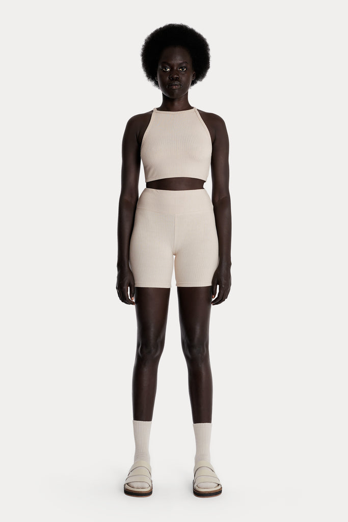 Model wearing sand ribbed biker shorts and a matching sand crop top, full-body front-side view.