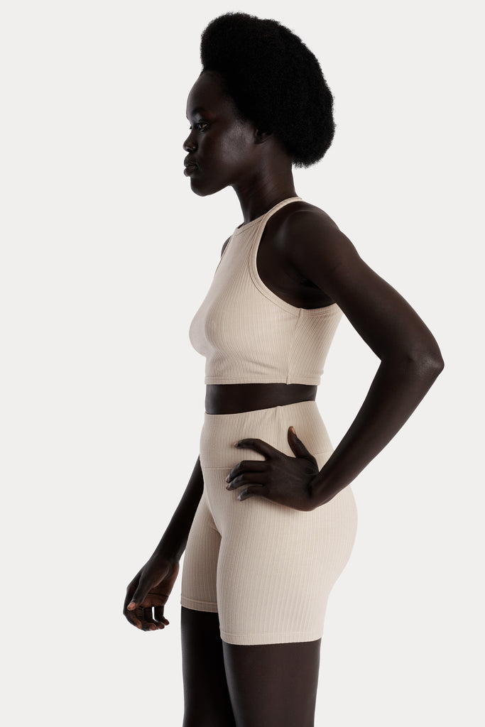 Model wearing sand ribbed biker shorts and a matching sand crop top, left-side close-up view.