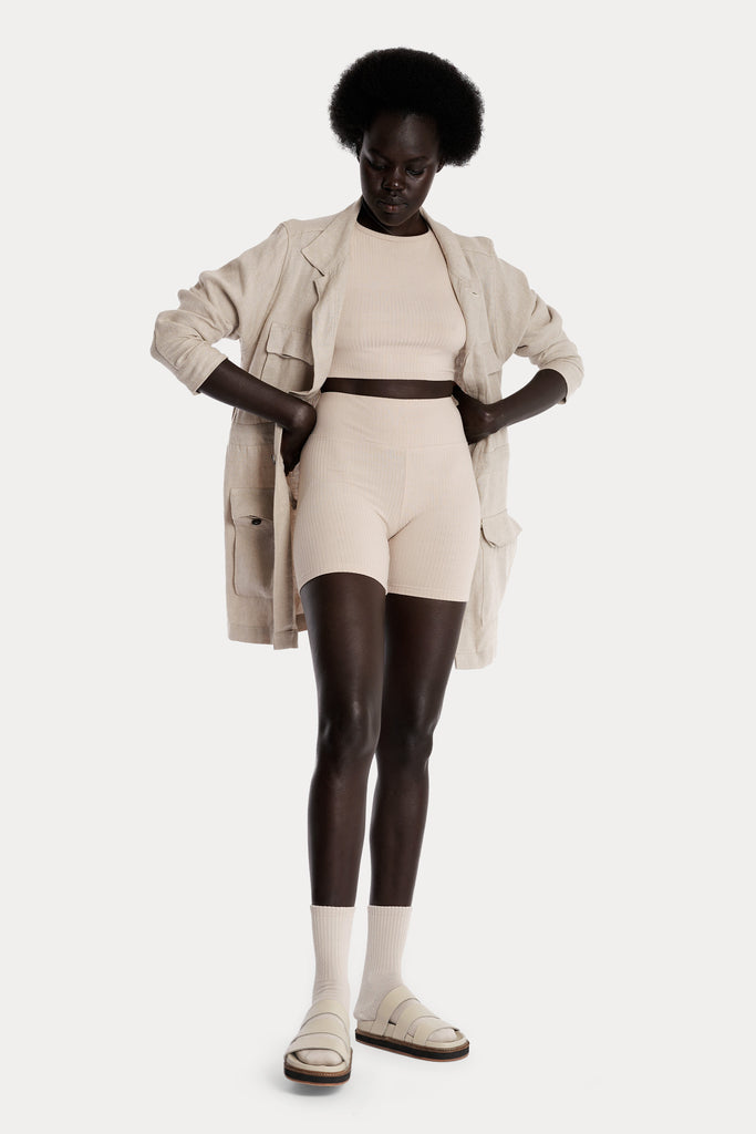 Model wearing sand ribbed biker shorts and a matching sand crop top, and a natural linen jacket, full-body front-side view.