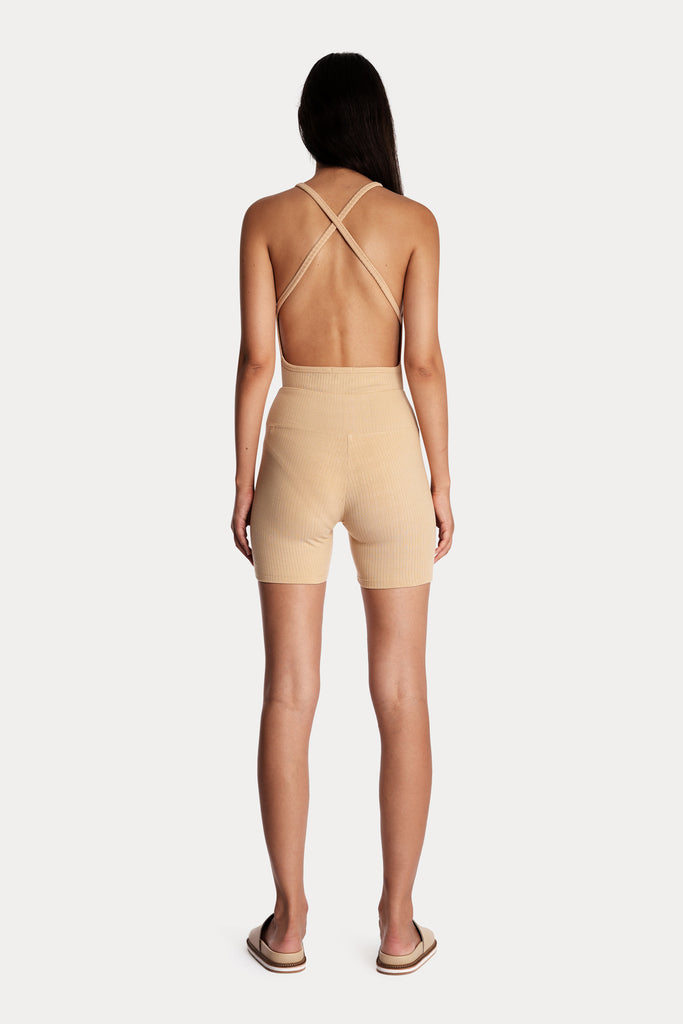 Model wearing tan ribbed biker shorts and a matching tan bodysuit, full-body back-side view.