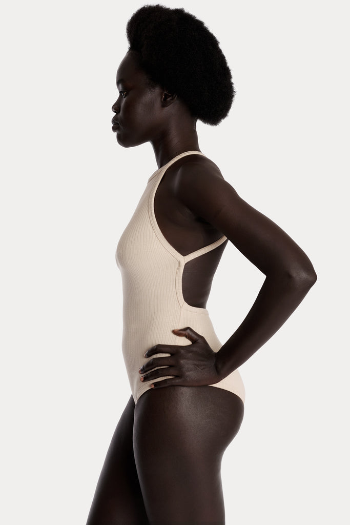 Model wearing a sand ribbed bodysuit left-side closeup.