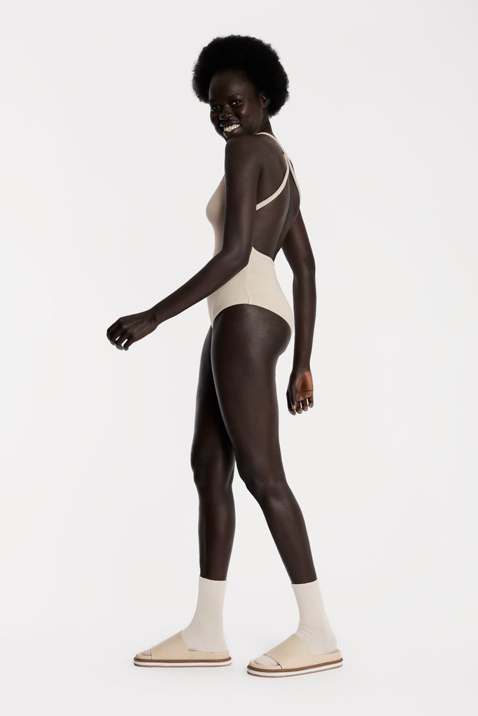 Model wearing a sand ribbed bodysuit full-body left-side closeup.