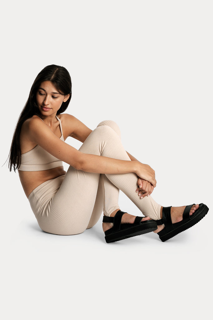 Model wearing a sand ribbed bralette and matching sand stirrup leggings, full-body right-side sitting on floor.