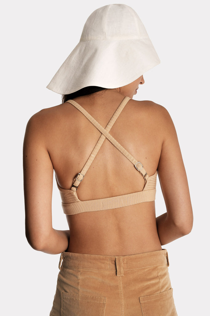 Model wearing a tan ribbed bralette and corduroy trousers, with white linen wide-brim hat, back-side close-up view.