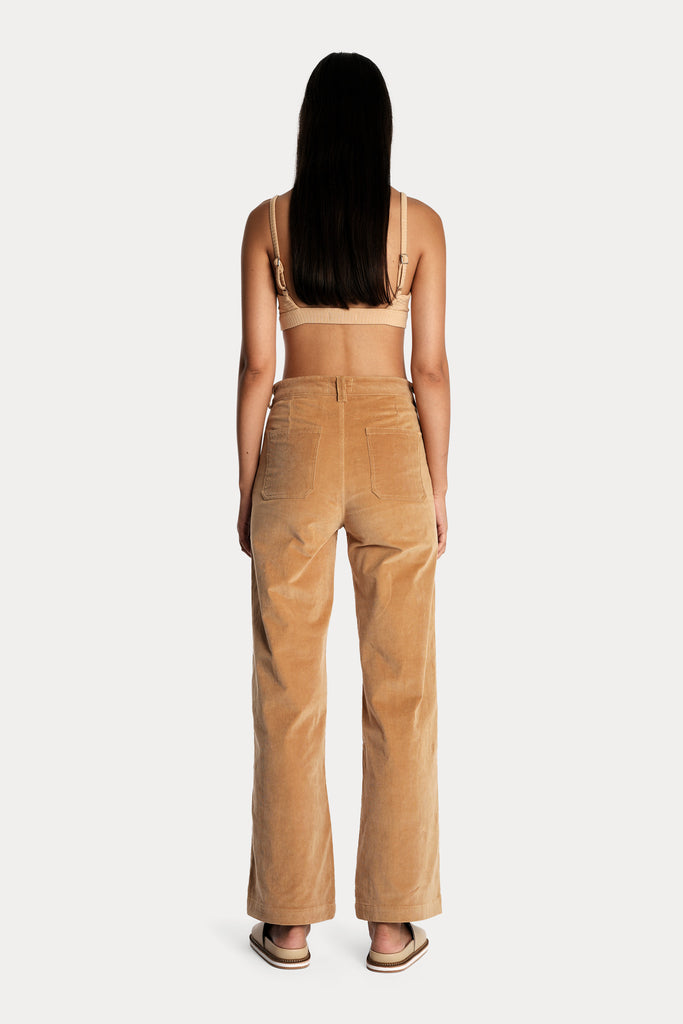 Model wearing a tan ribbed bralette and corduroy trousers, full-body back-side view.