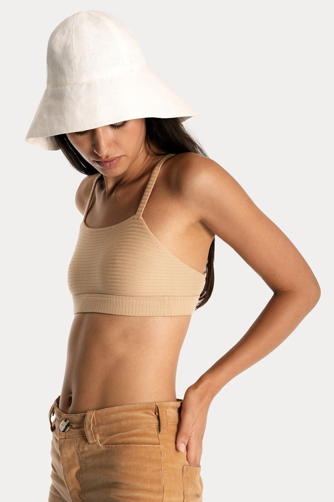 Model wearing a tan ribbed bralette and corduroy trousers, with white linen wide-brim hat, front-left close-up view.