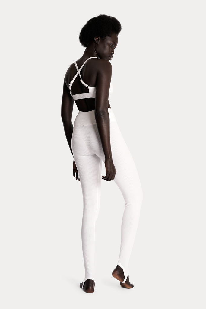 Model wearing a white ribbed bralette and matching white stirrup leggings, full-body back-right view.