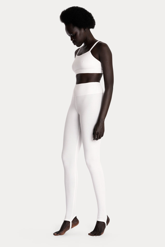 Model wearing a white ribbed bralette and matching white stirrup leggings, full-body front-left view.