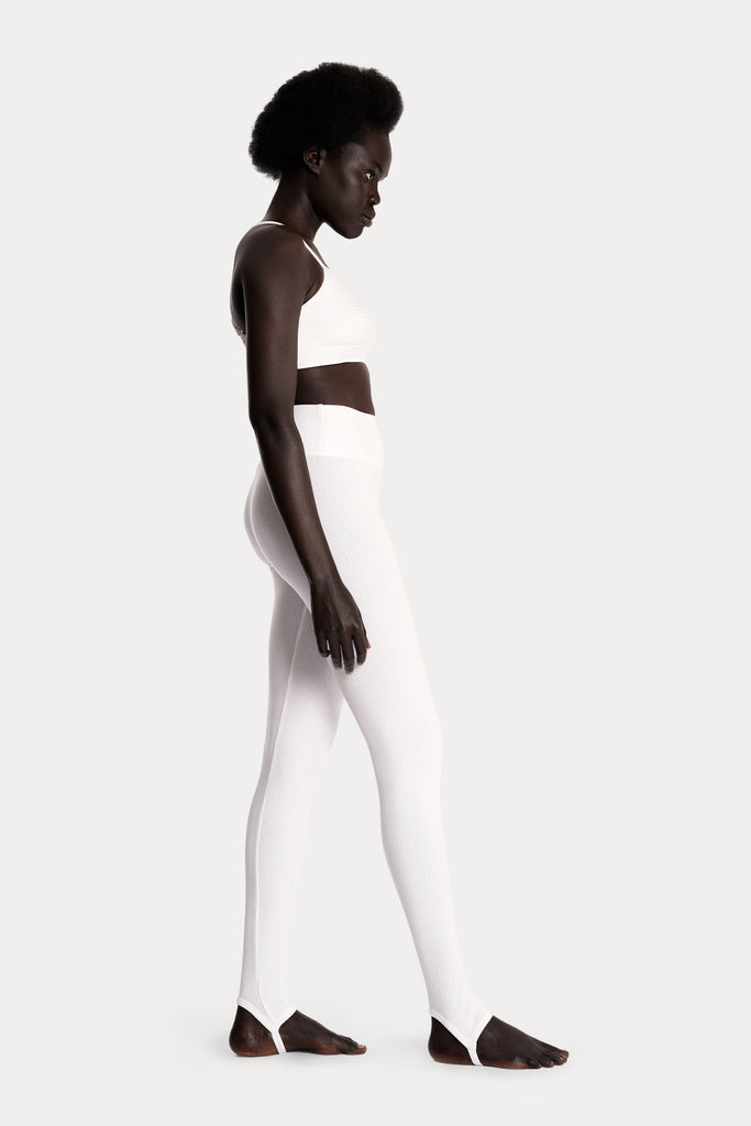Model wearing a white ribbed bralette and matching white stirrup leggings, full-body right-side view.