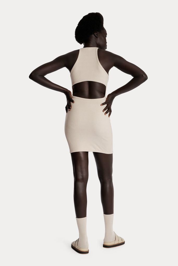 Model wearing a sand ribbed mini dress, full-body back-side view.