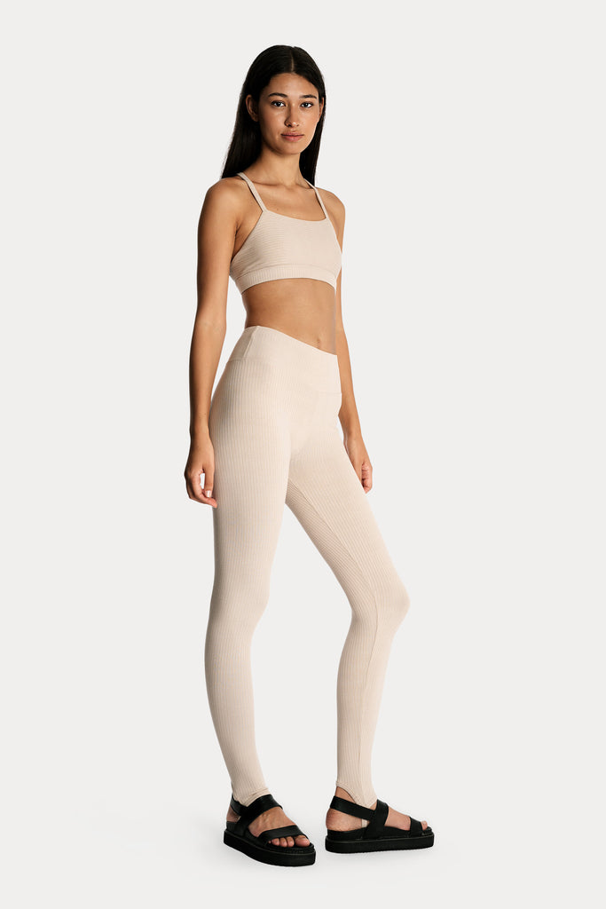 Model wearing sand ribbed stirrup leggings and matching sand bralette, full-body front-right view.