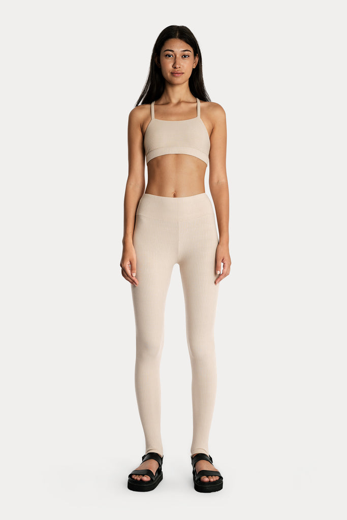 Model wearing sand ribbed stirrup leggings and a matching sand bralette, full-body front-side view.