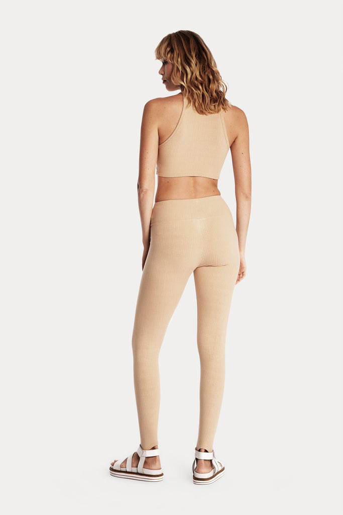 Model wearing tan ribbed stirrup leggings and a matching tan crop top, full-body back-side view.