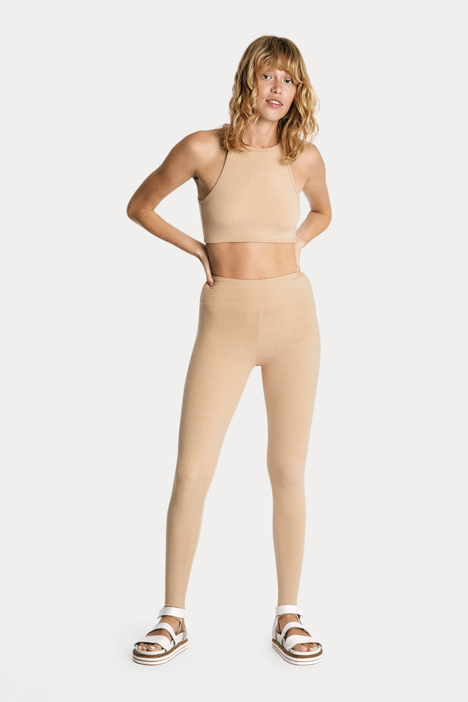 Model wearing tan ribbed stirrup leggings and a matching tan crop top, full-body front-side view.