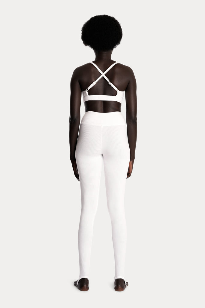 Model wearing white ribbed stirrup leggings and a matching white bralette, full-body back-side view.