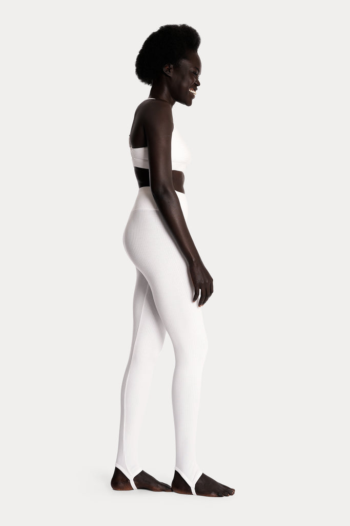 Model wearing white ribbed stirrup leggings and a matching white bralette, full-body right-side view.